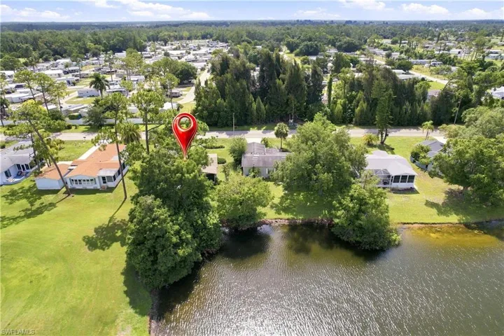 Waterfront property featuring a single-story residence with a screened lanai, mature trees, and a grassy expanse leading to the water's edge