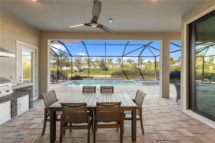 View of patio / terrace featuring exterior kitchen, a sunroom, outdoor dining space, and a pool with connected hot tub