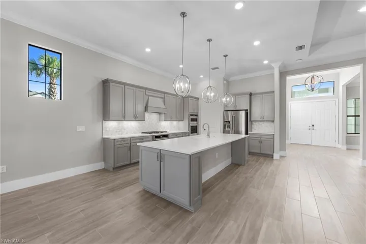 Kitchen featuring gray cabinetry, a chandelier, a kitchen bar, ornamental molding, and a kitchen island with sink