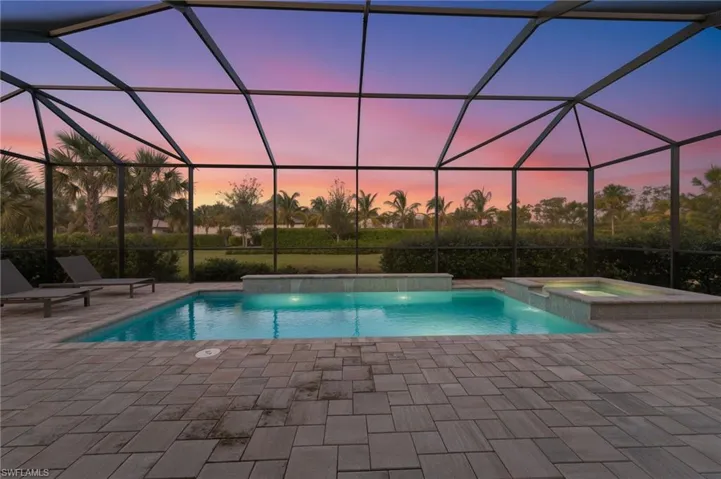 Pool at dusk featuring a sunroom, a lanai, a pool with connected hot tub, and a patio area