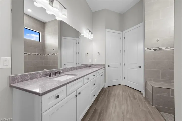 Bathroom with double vanity, light wood finished floors, and a walk in shower