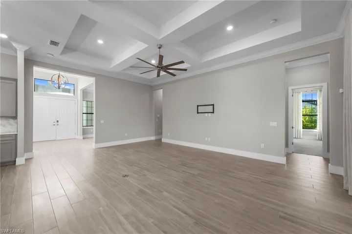 Unfurnished living room featuring ornamental molding, healthy amount of natural light, light wood finished floors, coffered ceiling, and recessed lighting