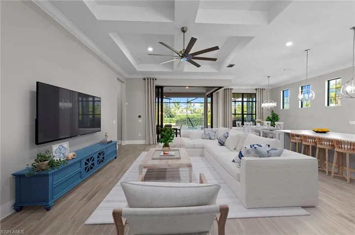 Living room with light wood finished floors, coffered ceiling, a ceiling fan, a chandelier, and recessed lighting