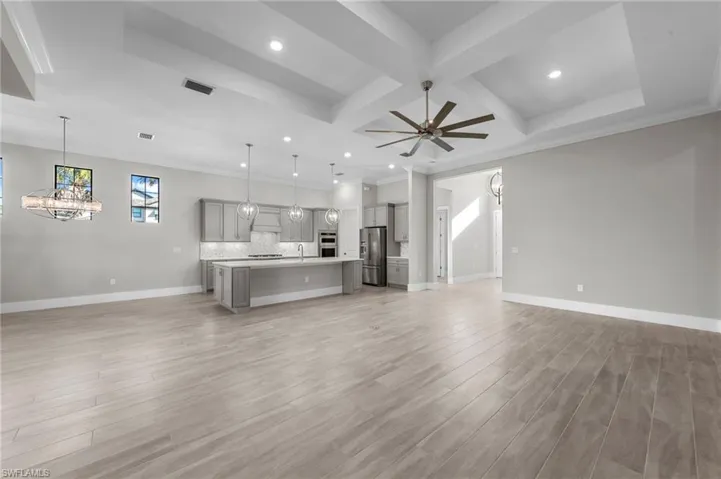 Unfurnished living room featuring a chandelier, coffered ceiling, light wood-style floors, recessed lighting, and beamed ceiling