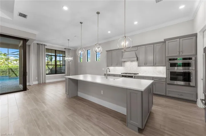 Kitchen with crown molding, gray cabinets, light wood-style floors, tasteful backsplash, and hanging light fixtures