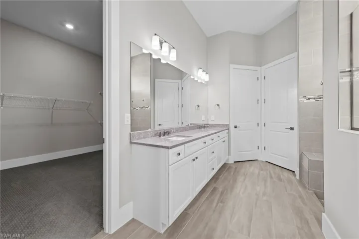 Full bath with a walk in closet, double vanity, walk in shower, and light wood-type flooring