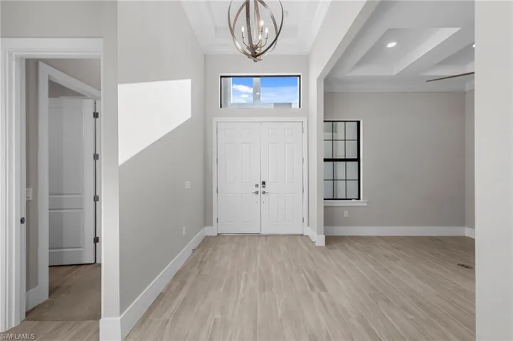 Entryway featuring light wood finished floors, ornamental molding, and a chandelier