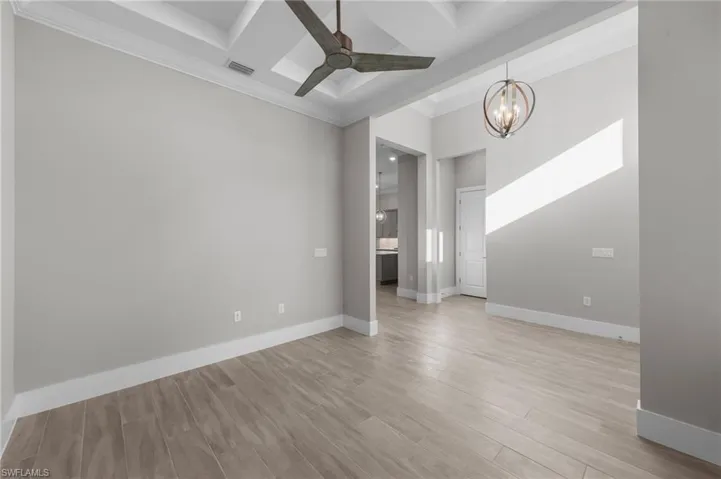 Spare room with coffered ceiling, a chandelier, beam ceiling, light wood-style flooring, and ceiling fan