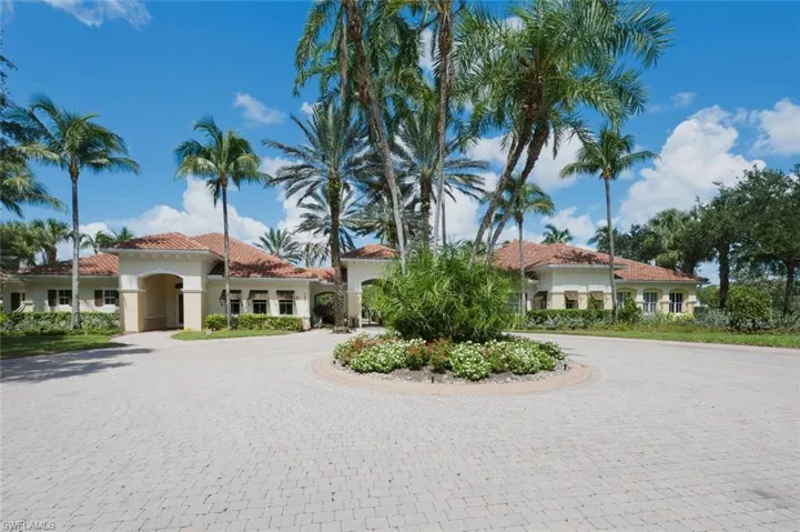Paver driveway with a central landscaped island, Spanish Colonial architecture, terracotta roof tiles, arched entryways, and lush tropical landscaping
