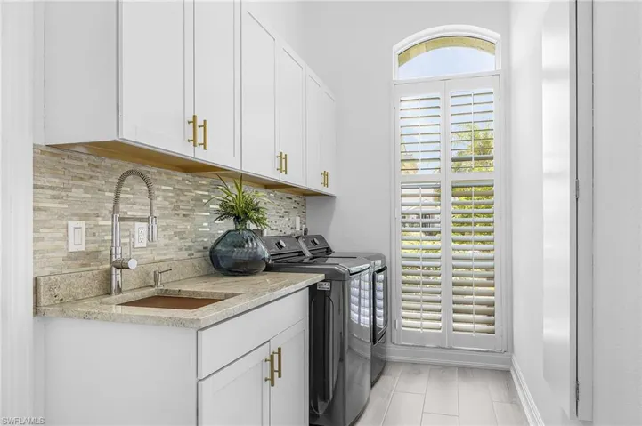 Laundry room featuring white shaker cabinetry with gold-finish hardware, a speckled stone countertop, and a built-in sink with a gooseneck faucet