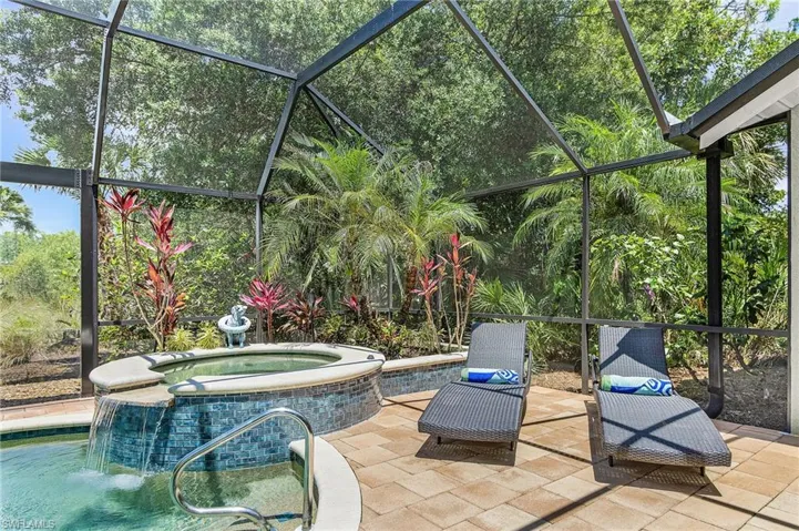 Screened outdoor lanai featuring a spa with a waterfall, blue mosaic tile accents, and a stone coping