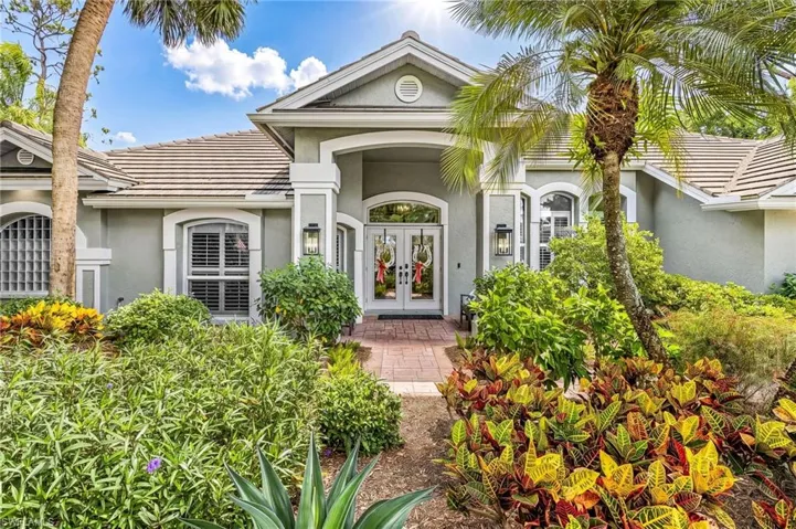 Front elevation featuring a double-door entry, arched windows, decorative exterior lighting, a tile roof, and lush tropical landscaping