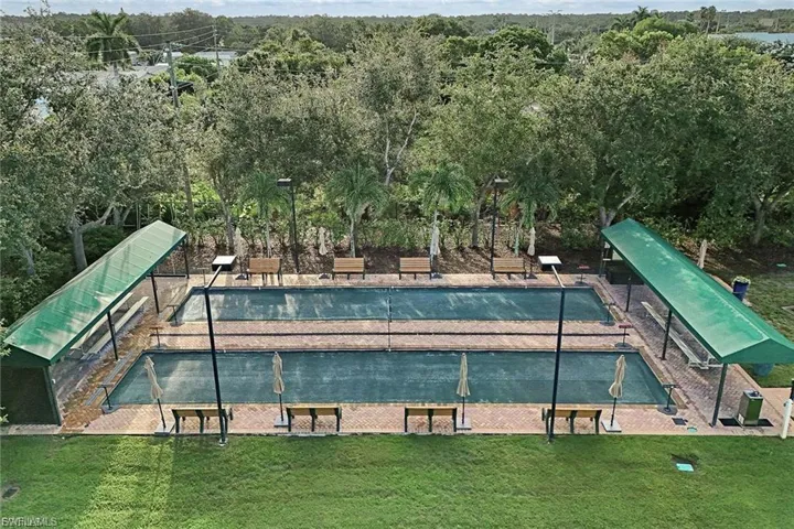 Two bocce ball courts featuring brick paver surrounds, covered seating areas with benches, and integrated lighting fixtures