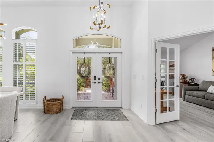 Bright entry foyer featuring double glass doors with an arched transom, high ceilings, a contemporary chandelier, and wood-finish flooring