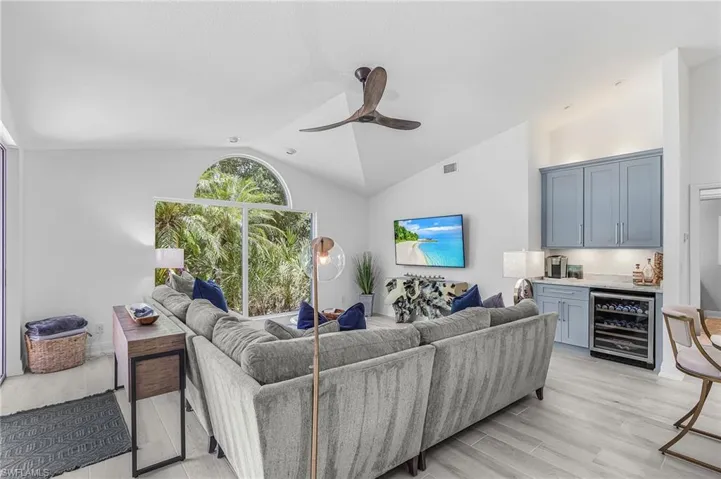 Family room featuring vaulted ceilings, an arched window, wood-finish flooring, a built-in wet bar with cabinetry, and a beverage cooler