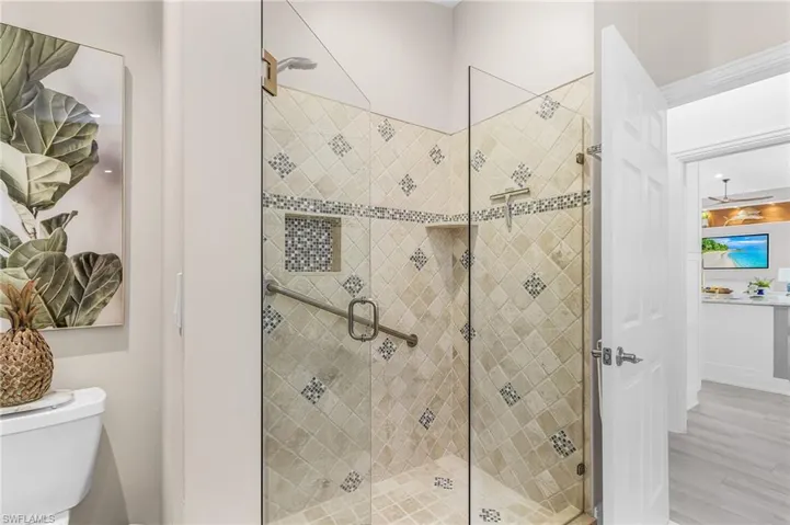 Glass-enclosed shower with decorative tiled walls, built-in shower niche, and a grab bar
