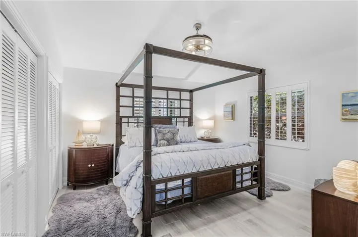 Guest Bedroom 1 light wood-finish tile flooring, white walls, plantation shutters, and a lighted ceiling fan