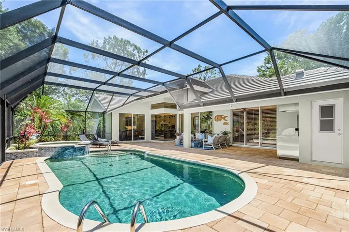 Screen-enclosed pool area featuring a freeform swimming pool with integrated spa and waterfall, a paver deck, and exterior access to the home