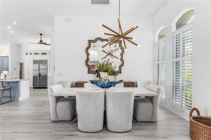 Dining area featuring high ceilings, a contemporary chandelier, two arched transom windows, plantation shutters, and light wood-finish flooring