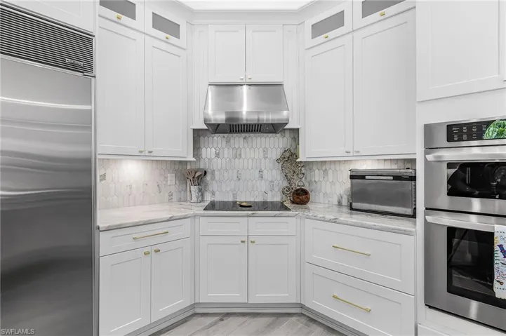 Gourmet kitchen featuring stainless steel appliances, white shaker cabinetry with gold-tone hardware, and a unique elongated hexagonal tile backsplash