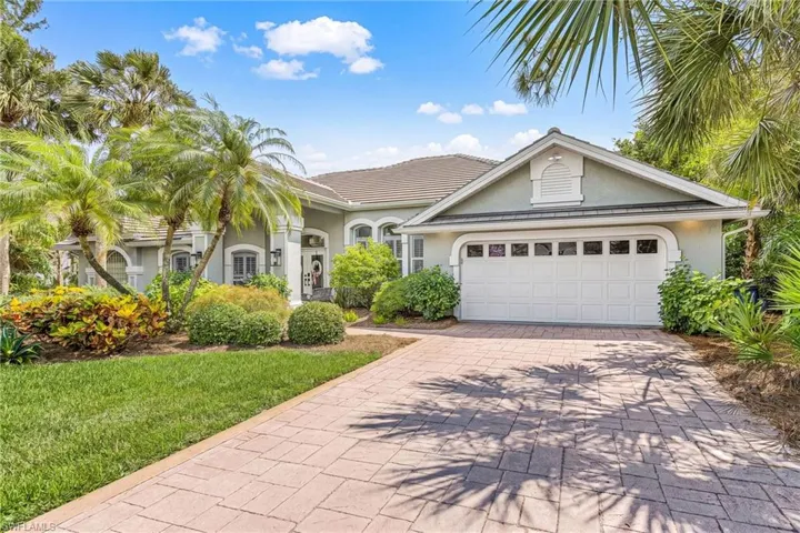 Contemporary residence featuring a paved driveway, a two-car garage with panel windows, a tiled roof, and a meticulously landscaped front yard with mature palm trees