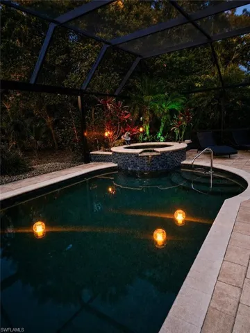 Screened pool enclosure featuring a dark-bottom pool with a stone coping and paver decking