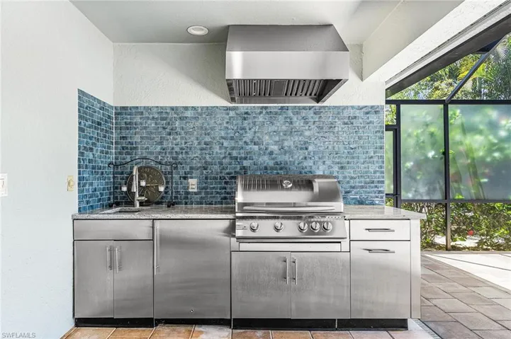 Outdoor kitchen featuring a stainless steel grill, large vent hood, sink, beverage fridge, coordinating cabinetry, and a blue tile backsplash