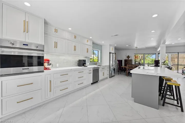 Kitchen featuring appliances with stainless steel finishes, light marble finish flooring, decorative backsplash, a kitchen breakfast bar, and white cabinetry