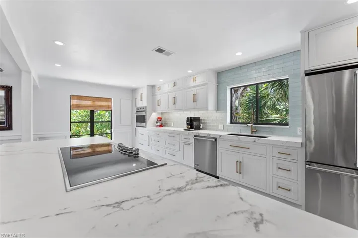 Kitchen featuring appliances with stainless steel finishes, backsplash, light stone countertops, recessed lighting, and white cabinets