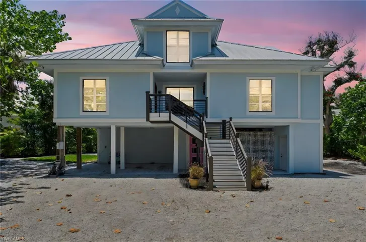 View of front facade with a metal roof, a carport, stairway, and driveway