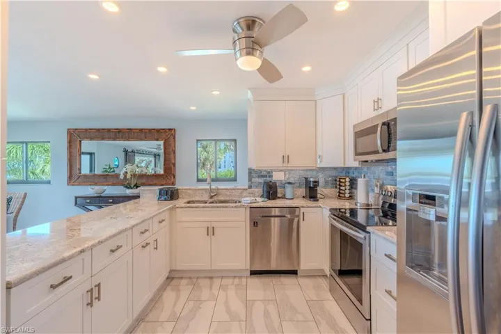 Kitchen with stainless steel appliances, light stone counters, white cabinetry, decorative backsplash, and recessed lighting - Virtually Edited Image