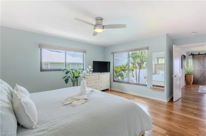Bedroom featuring a barn door, multiple windows, light wood-style flooring, and a ceiling fan - Virtually Edited Image