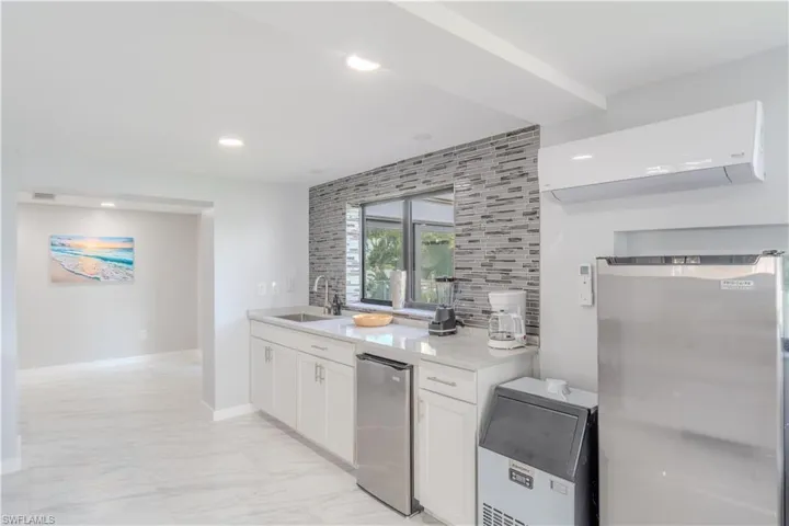 Kitchen with white cabinetry, backsplash, a wall unit AC, light stone counters, and recessed lighting - Virtually Edited Image