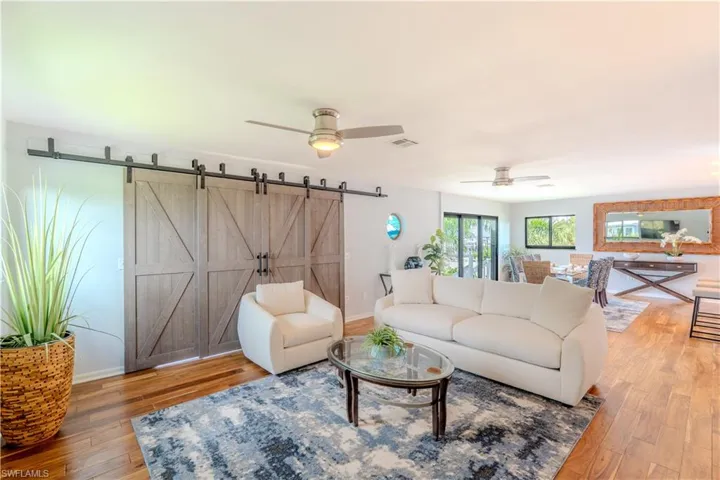 Living room with ceiling fan, wood finished floors, and a barn door - Virtually Edited Image