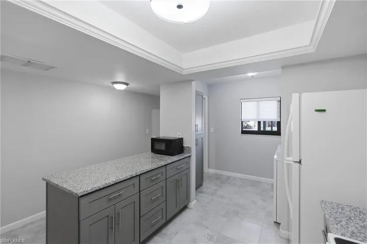 Kitchen with freestanding refrigerator, light stone countertops, black microwave, a peninsula, and gray cabinetry
