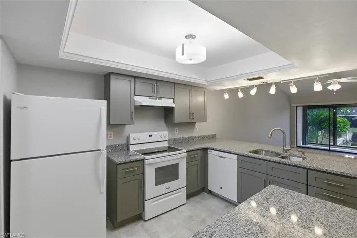 Kitchen featuring white appliances, light stone countertops, gray cabinets, a tray ceiling, and under cabinet range hood