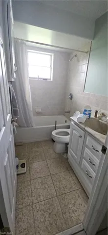 Full bathroom with vanity, shower / tub combo with curtain, toilet, and tile patterned flooring