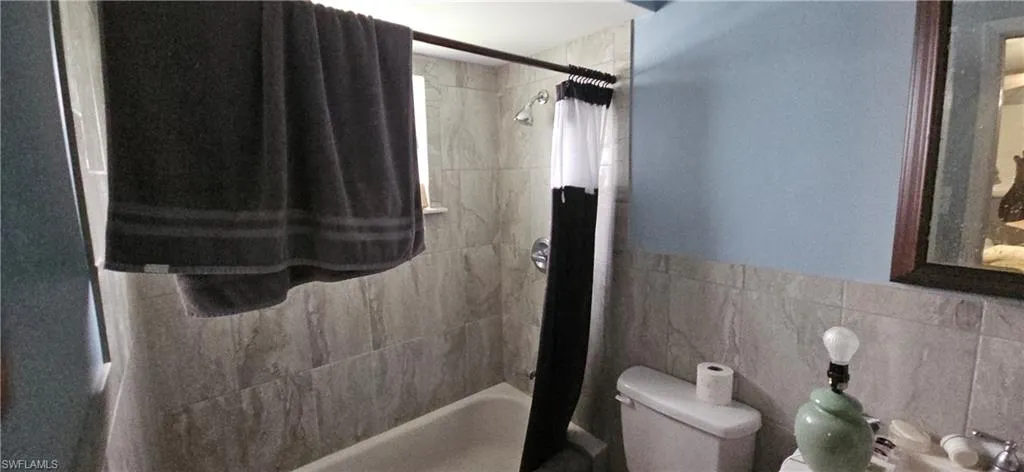 Bathroom with toilet, shower / bath combo, and tile walls