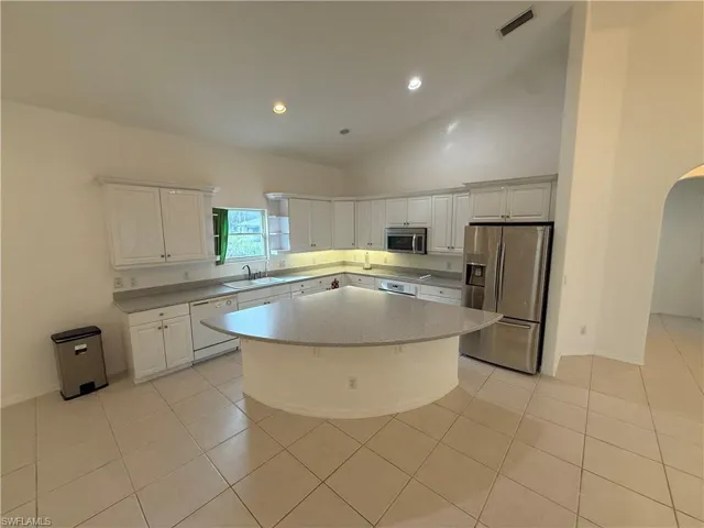 Kitchen with appliances with stainless steel finishes, white cabinets, arched walkways, recessed lighting, and light tile patterned flooring