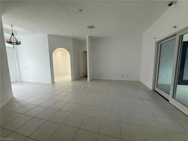 Unfurnished room featuring arched walkways, a chandelier, and light tile patterned flooring