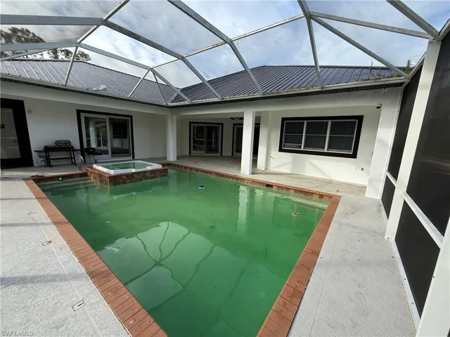 View of swimming pool featuring a sunroom, a pool with connected hot tub, a patio area, and glass enclosure