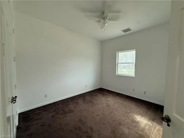 Empty room featuring dark carpet and ceiling fan