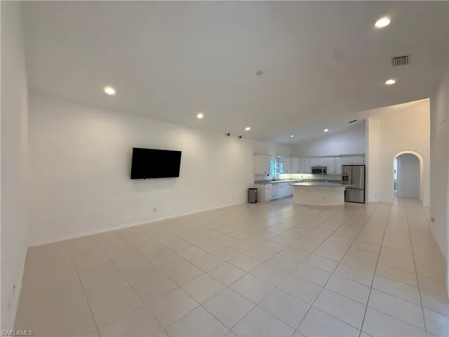 Unfurnished living room featuring arched walkways, recessed lighting, light tile patterned flooring, and high vaulted ceiling