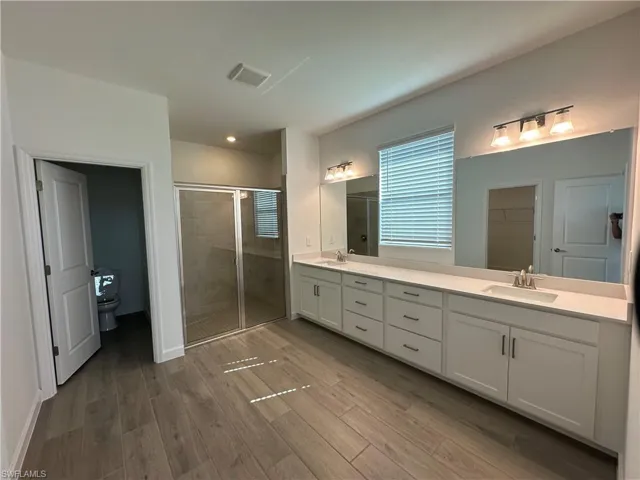 Bathroom featuring oversized vanity, toilet, hardwood / wood-style floors, an enclosed shower, and double sink