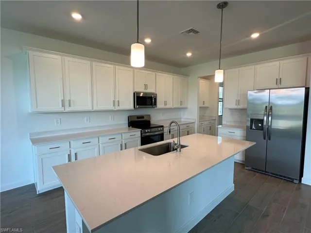 Kitchen featuring hanging light fixtures, a kitchen island with sink, white cabinetry, and appliances with stainless steel finishes