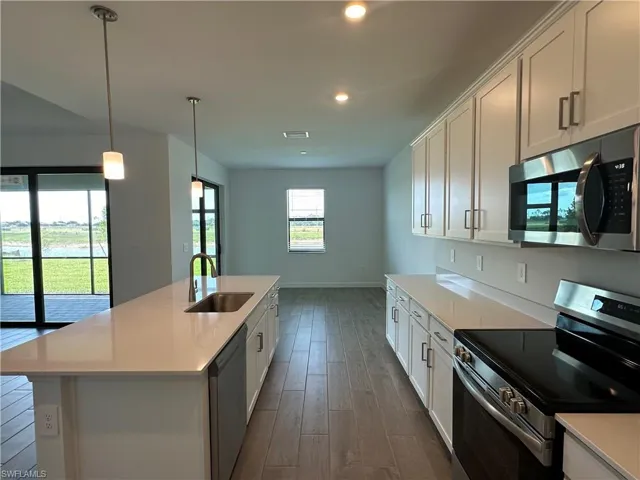Kitchen featuring stainless steel appliances, a center island with sink, sink, and dark wood-type flooring