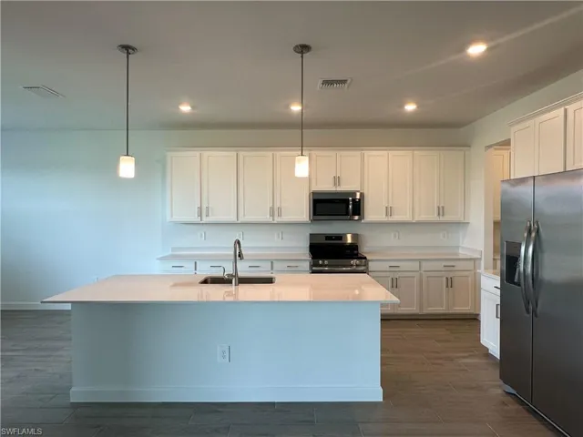 Kitchen with hanging light fixtures, a center island with sink, appliances with stainless steel finishes, white cabinets, and sink