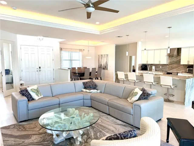 Living area featuring ceiling fan, ornamental molding, a tray ceiling, light wood-type flooring, and recessed lighting
