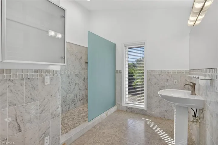 Bathroom featuring tile walls, a wainscoted wall, a walk in shower, and tile patterned floors