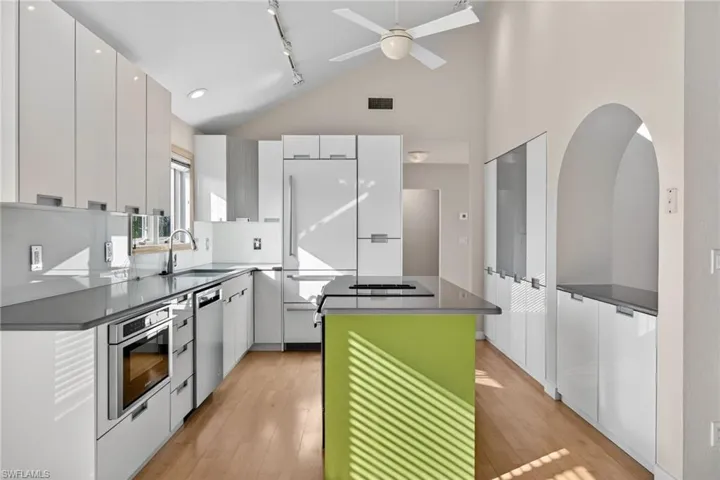 Kitchen featuring modern cabinets, a kitchen island, rail lighting, white cabinets, and high vaulted ceiling